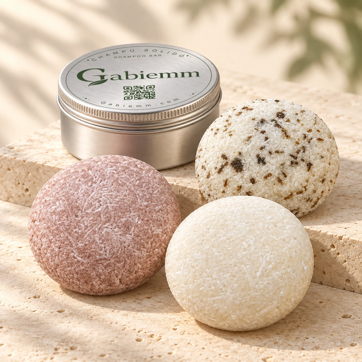 Los tres champús sólidos Gabiemm, rosado de cebolla, blanco marfil de levadura y blanco con partículas oscuras de cade, junto a la lata definitiva cerrada sobre piedra clara.